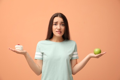 Woman choosing between apple and cake on orange background