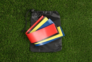 Bag with fitness elastic bands on green grass, top view