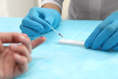 Doctor testing blood sample from patient's finger at table, closeup