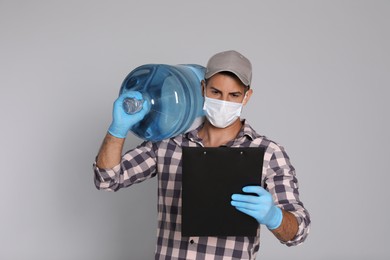 Courier in medical mask with bottle for water cooler and clipboard on light grey background. Delivery during coronavirus quarantine