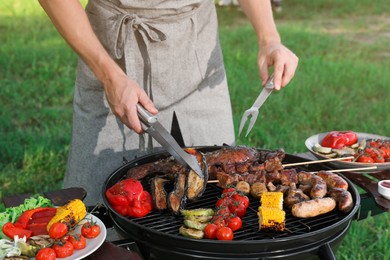 Photo of Man cooking meat and vegetables on barbecue grill outdoors, closeup