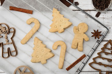 Photo of Christmas treat. Flat lay composition with cookie cutters and baked biscuits on white wooden table