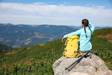 Tourist with backpack and trekking poles enjoying mountain landscape on rocky peak, back view