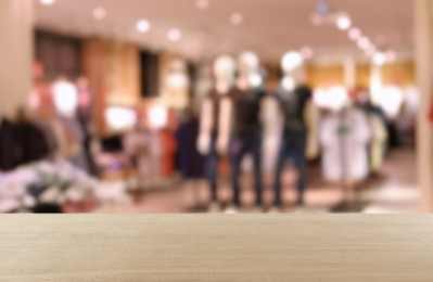 Empty wooden table and blurred view of store with modern clothes