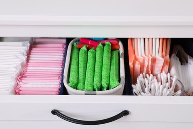 Open cabinet drawer with menstrual pads, tampons and cotton buds, closeup