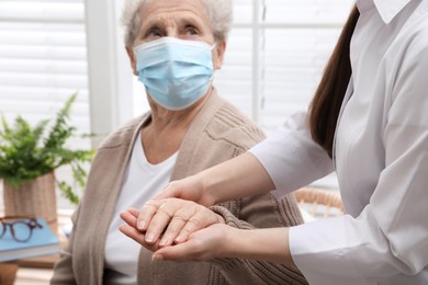 Doctor taking care of senior woman with protective mask at nursing home, focus on hands
