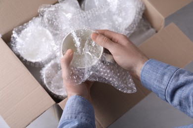 Photo of Man covering ceramic dishware with bubble wrap, closeup