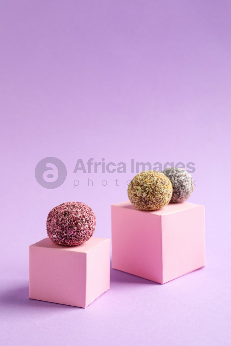 Photo of Minimalistic composition with different delicious vegan candy balls and pink cubes on violet background