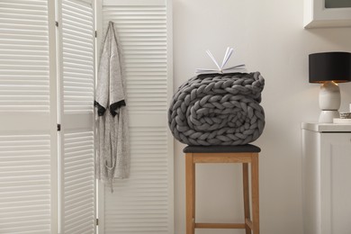 Wooden stool with rolled chunky knit blanket and book in room