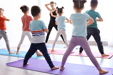 Little children and their teacher practicing yoga in gym