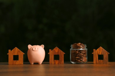 Photo of Piggy bank, jar of coins and house models on wooden table