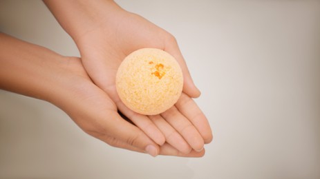 Photo of Woman holding bath bomb on light background, closeup. Space for text