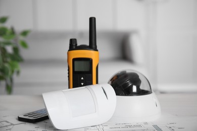 Photo of CCTV camera, remote control, movement detector and walkie talkie on building plan indoors. Home security system