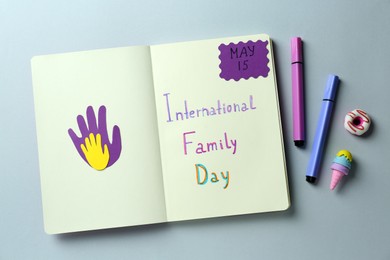 Photo of Notebook with text International Family Day May, paper hand cutouts and stationery on light grey background, flat lay