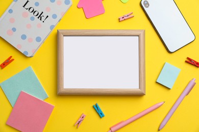Blank white board with stationery and smartphone on yellow background, flat lay. Space for text