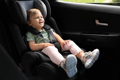 Cute little girl sitting in child safety seat inside car