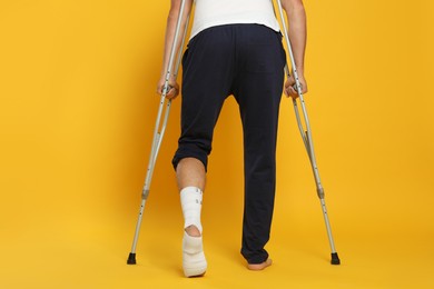 Man with injured leg using crutches on yellow background, closeup