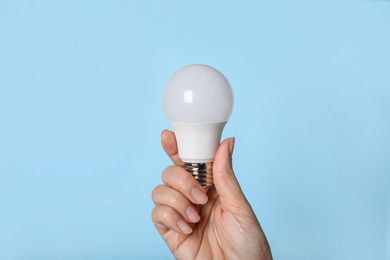 Woman holding LED light bulb on blue background, closeup