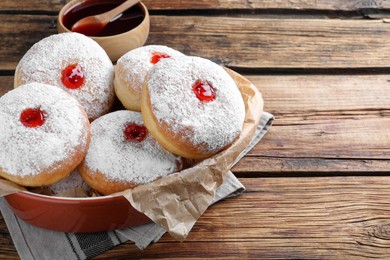 Delicious donuts with jelly and powdered sugar in baking dish on wooden table. Space for text