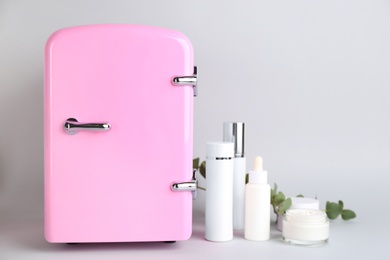 Cosmetic refrigerator and skin care products on light background