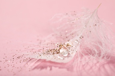 Closeup view of beautiful feather with dew drops and glitter on pink background