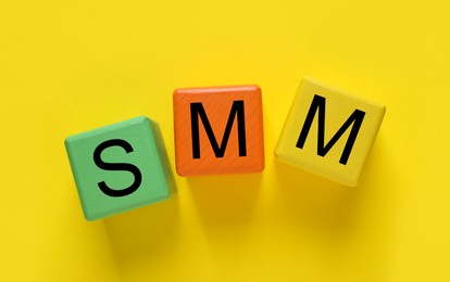 Colorful cubes with abbreviation SMM (Social media marketing) on yellow background, flat lay