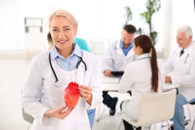 Female doctor holding heart model in clinic. Cardiology center
