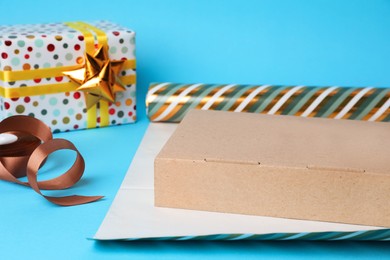 Roll of wrapping paper, box, ribbon and gift on light blue background