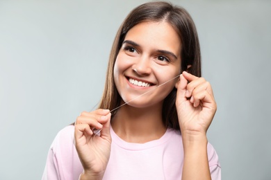 Young woman flossing her teeth on light grey background. Cosmetic dentistry