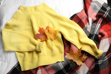 Photo of Beautiful yellow warm sweater, leaves and plaid on white bedsheet, flat lay