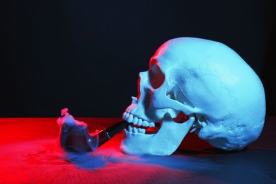 Photo of Human skull with pipe and smoke in neon lights on black background
