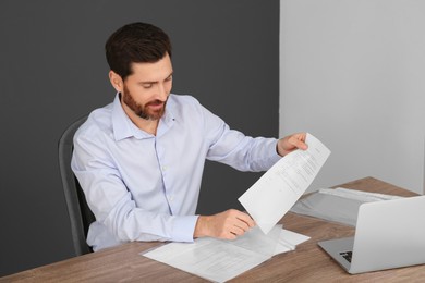 Photo of Businessman putting document into punched pocket at wooden table in office