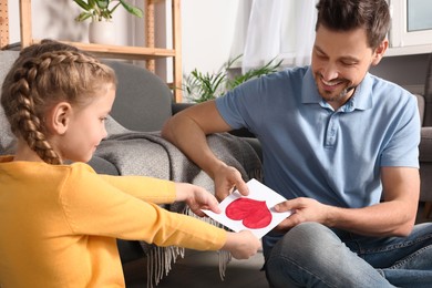 Photo of Happy man receiving greeting card from his little daughter at home