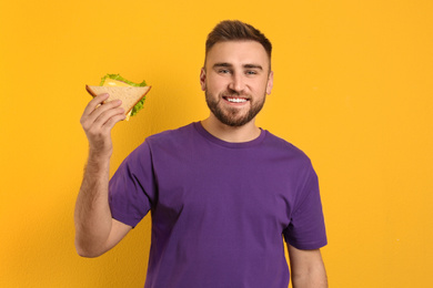 Photo of Young man with tasty sandwich on yellow background