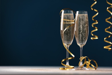 Glasses of champagne and serpentine streamers on table against dark blue background. Space for text