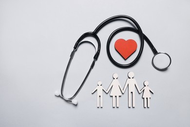 Photo of Figures of family near stethoscope and heart on white background, flat lay. Insurance concept