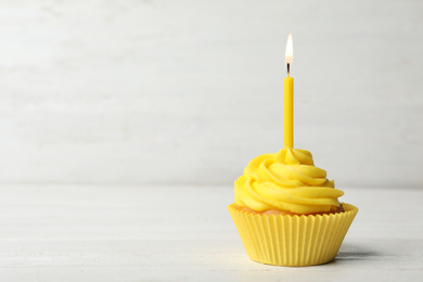 Delicious birthday cupcake with cream and burning candle on white wooden table. Space for text