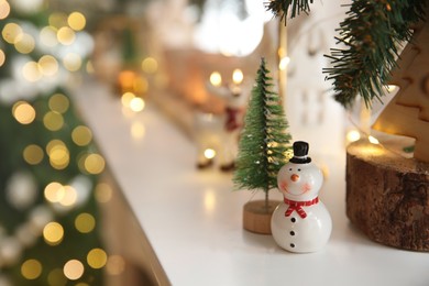 Funny ceramic snowman and small decorative tree on white table against blurred lights. Space for text