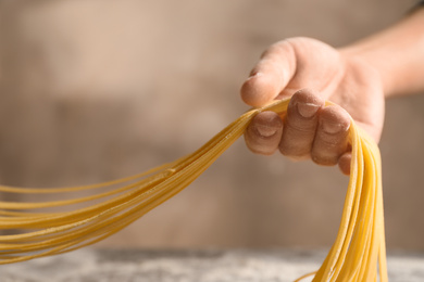 Woman holding noodles on light brown background, closeup. Italian pasta