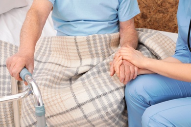 Nurse holding senior patient's hand in hospital, closeup. Medical assisting