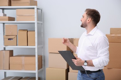 Young businessman with clipboard near cardboard boxes at warehouse