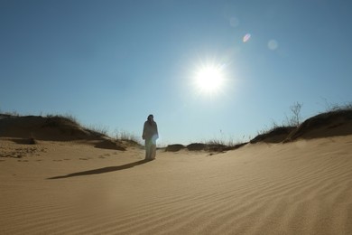 Man in arabic clothes walking through desert on sunny day, back view