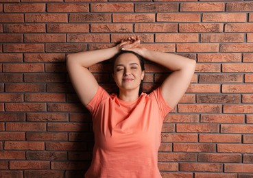 Photo of Happy overweight woman near red brick wall