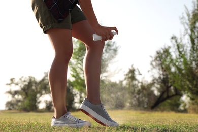 Woman applying insect repellent onto leg in park, closeup. Space for text