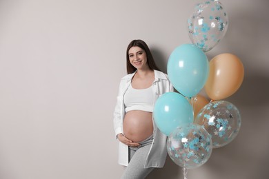 Happy pregnant woman with balloons near grey wall. Baby shower party