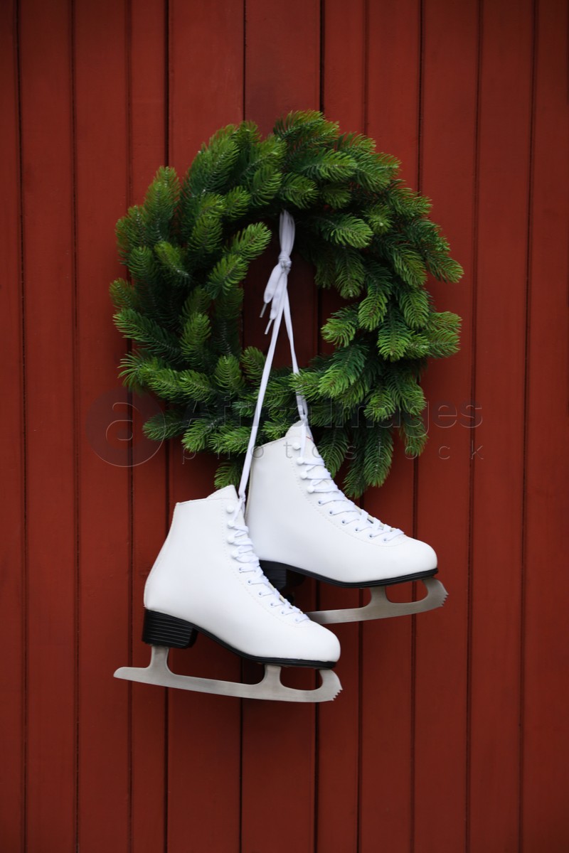 Pair of ice skates and beautiful Christmas wreath hanging on red wooden wall