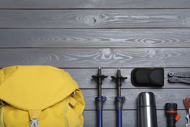 Flat lay composition with trekking poles and other hiking equipment on grey wooden background, space for text