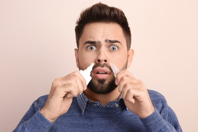 Man using nasal sprays on beige background