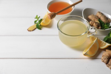 Photo of Delicious ginger tea and ingredients on white wooden table, space for text