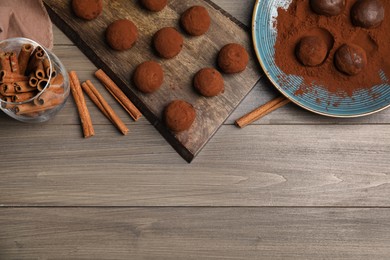 Delicious chocolate truffles with cocoa powder and cinnamon on wooden table, flat lay. Space for text